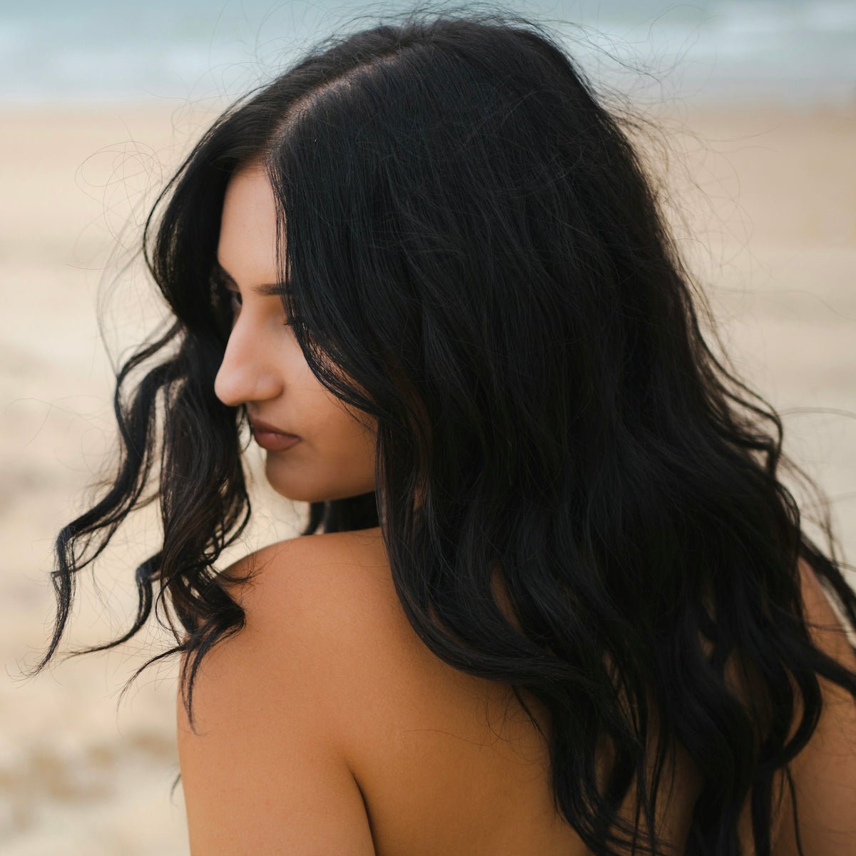 a woman with long black hair standing on a beach